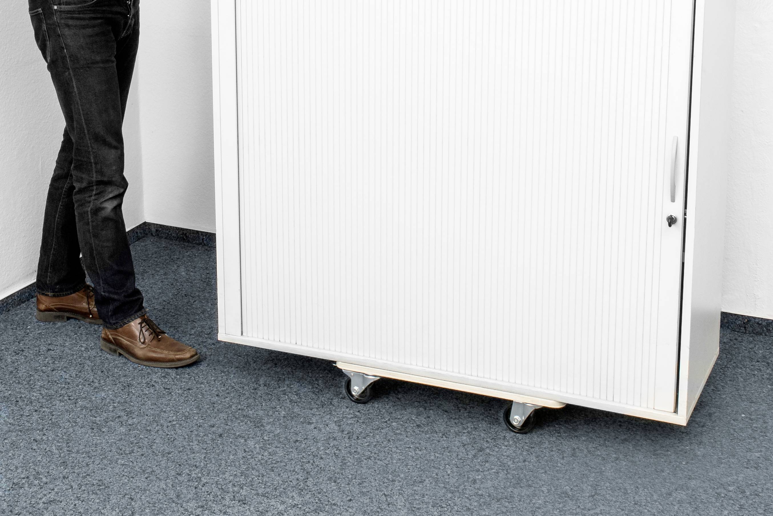 Een persoon staat naast een witte verrijdbare kast met gesloten rolluik op blauwe vloerbedekking.