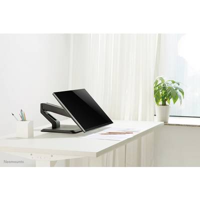 Een moderne bureau met een scherm op een verstelbare arm, naast een potje met pennen en een plant bij het raam.