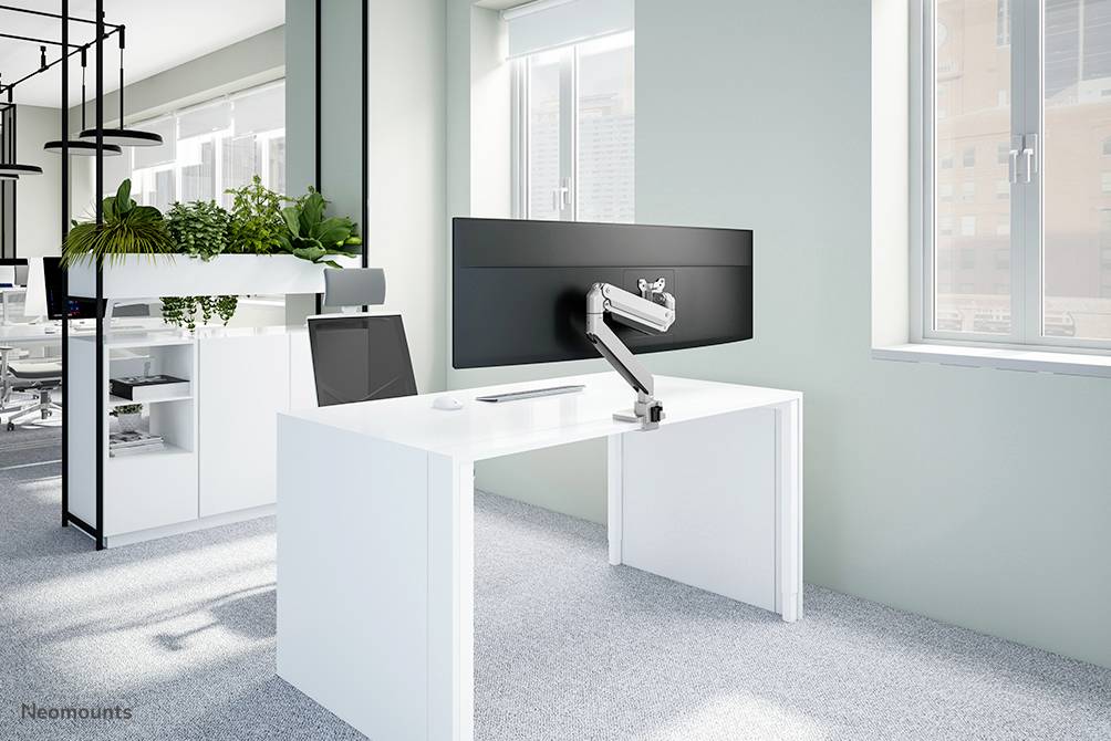 Een moderne kantoorruimte met een wit bureau, waarop een groot scherm is gemonteerd op een verstelbare arm, omringd door planten.