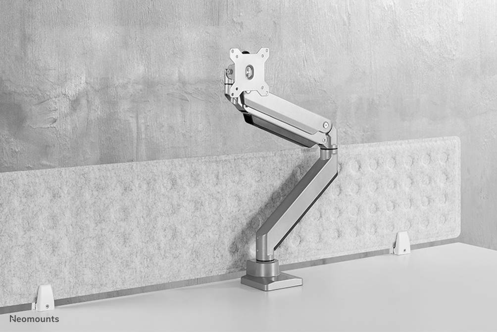 Ergonomische monitorarm van aluminium, bevestigd aan een tafelrand, in hoogte en hoek verstelbaar, voor een betonnen muur.