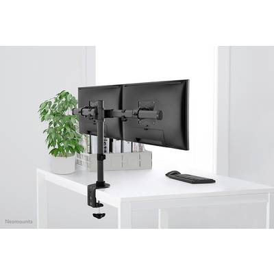 Een bureau met twee naast elkaar gemonteerde monitors, een toetsenbordset eronder, een plant links, in een lichte ruimte.