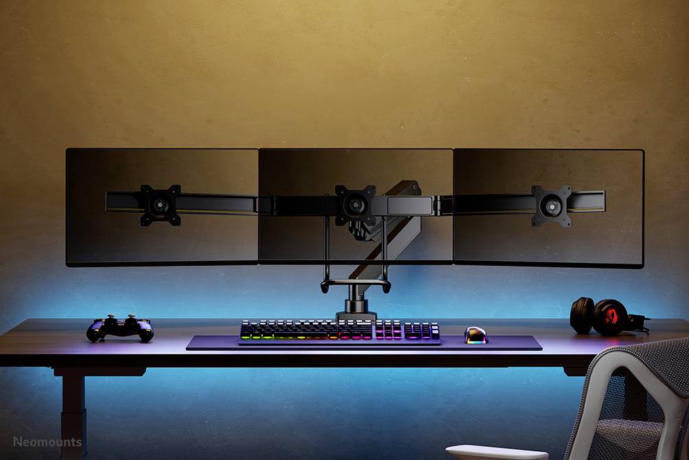 Een bureau met drie monitoren op een standaard, een RGB-toetsenbord, een muis, een controller en een headset.