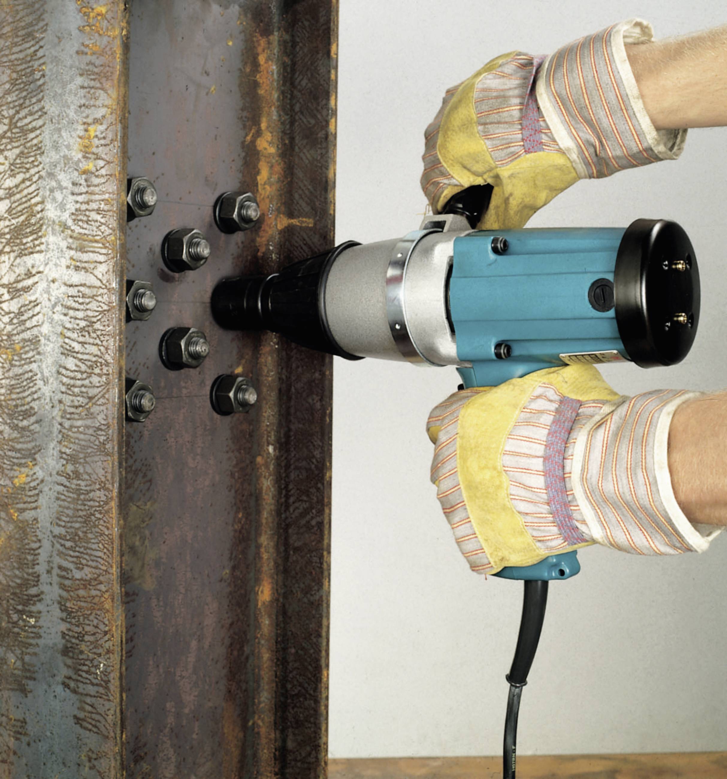 'Een persoon boort gaten in een metalen plaat met een elektrische boormachine. De persoon draagt gestreepte handschoenen.'