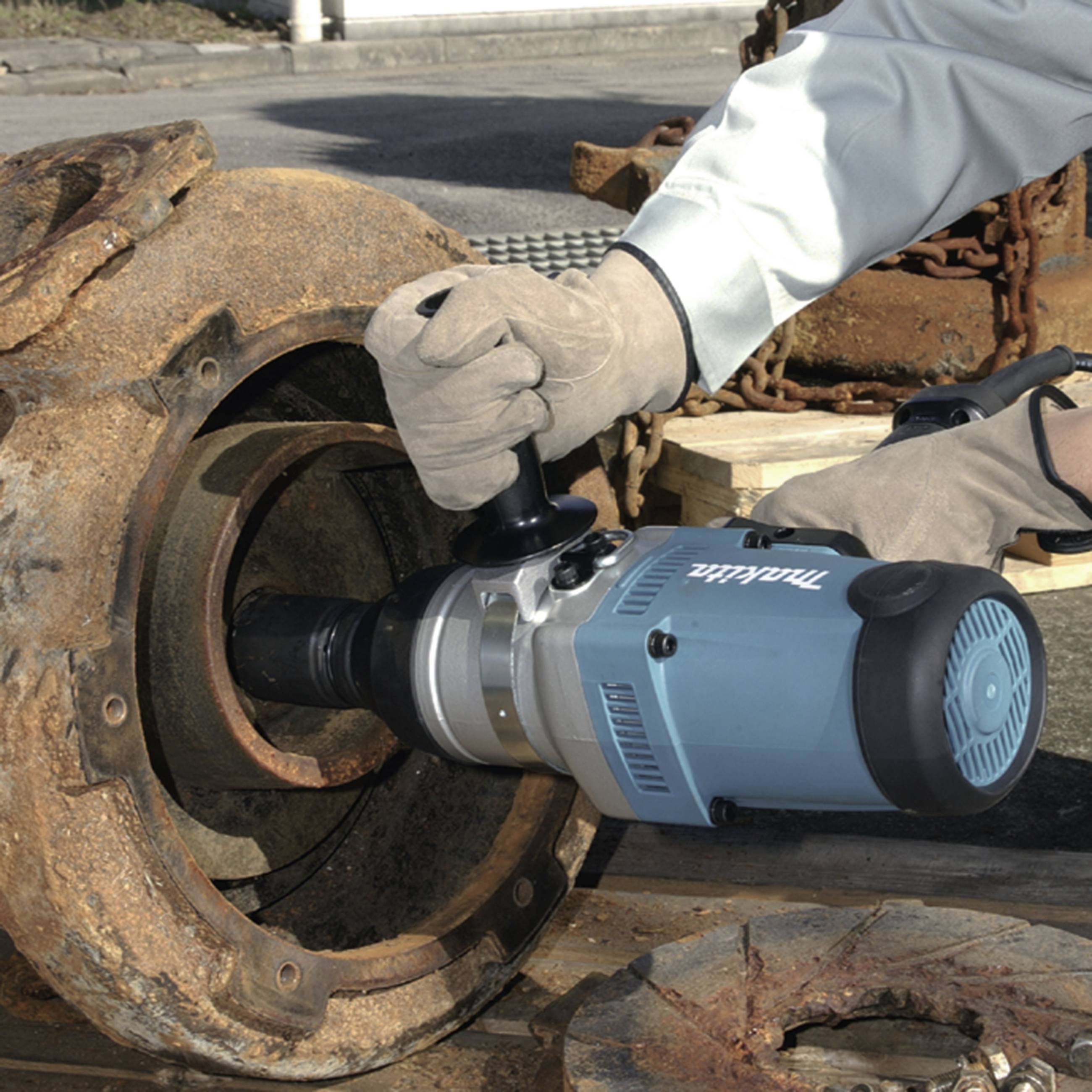 Een persoon gebruikt een elektrisch gereedschap om een grote, roestige metalen constructie te bewerken. De omgeving heeft een industriële uitstraling.