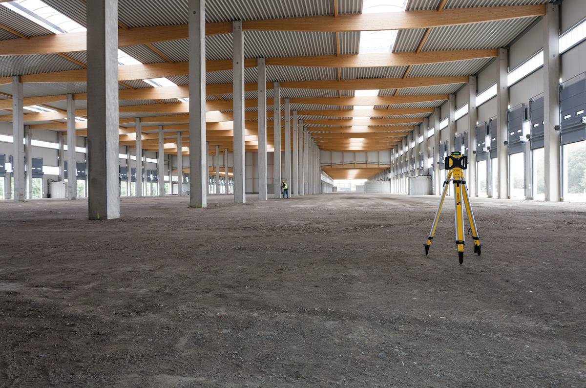 Een lege, grote binnenruimte met betonnen zuilen en houten balken aan het plafond. Een meetinstrument staat op de voorgrond.