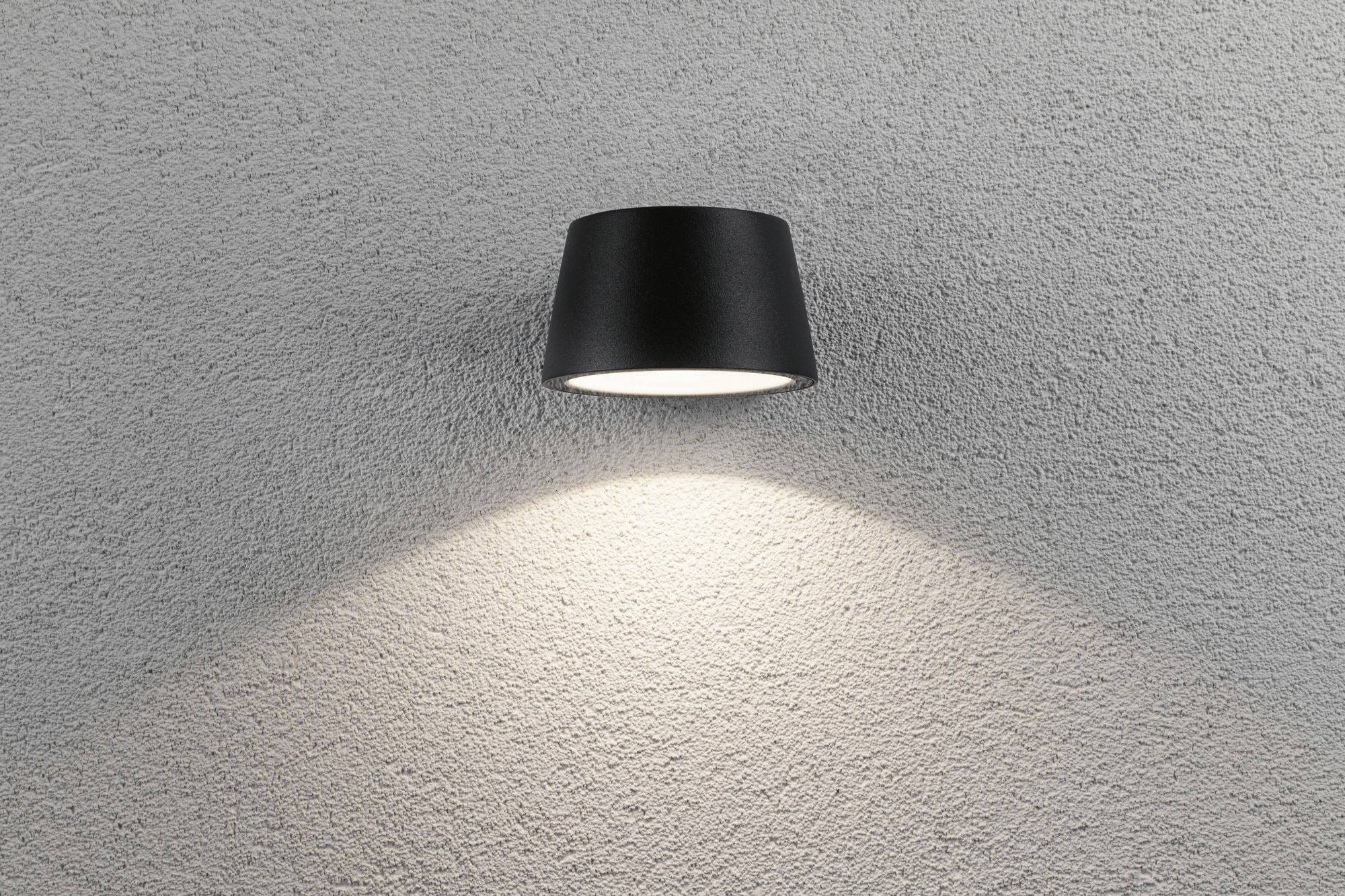 Zwarte wandlamp straalt licht naar beneden op een grijze muur, creëert een kegelvormige lichtbundel.