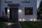 Moderne entree bij schemering, verlicht door wandlampen en padverlichting, met een pad op de voorgrond en ramen op de achtergrond.