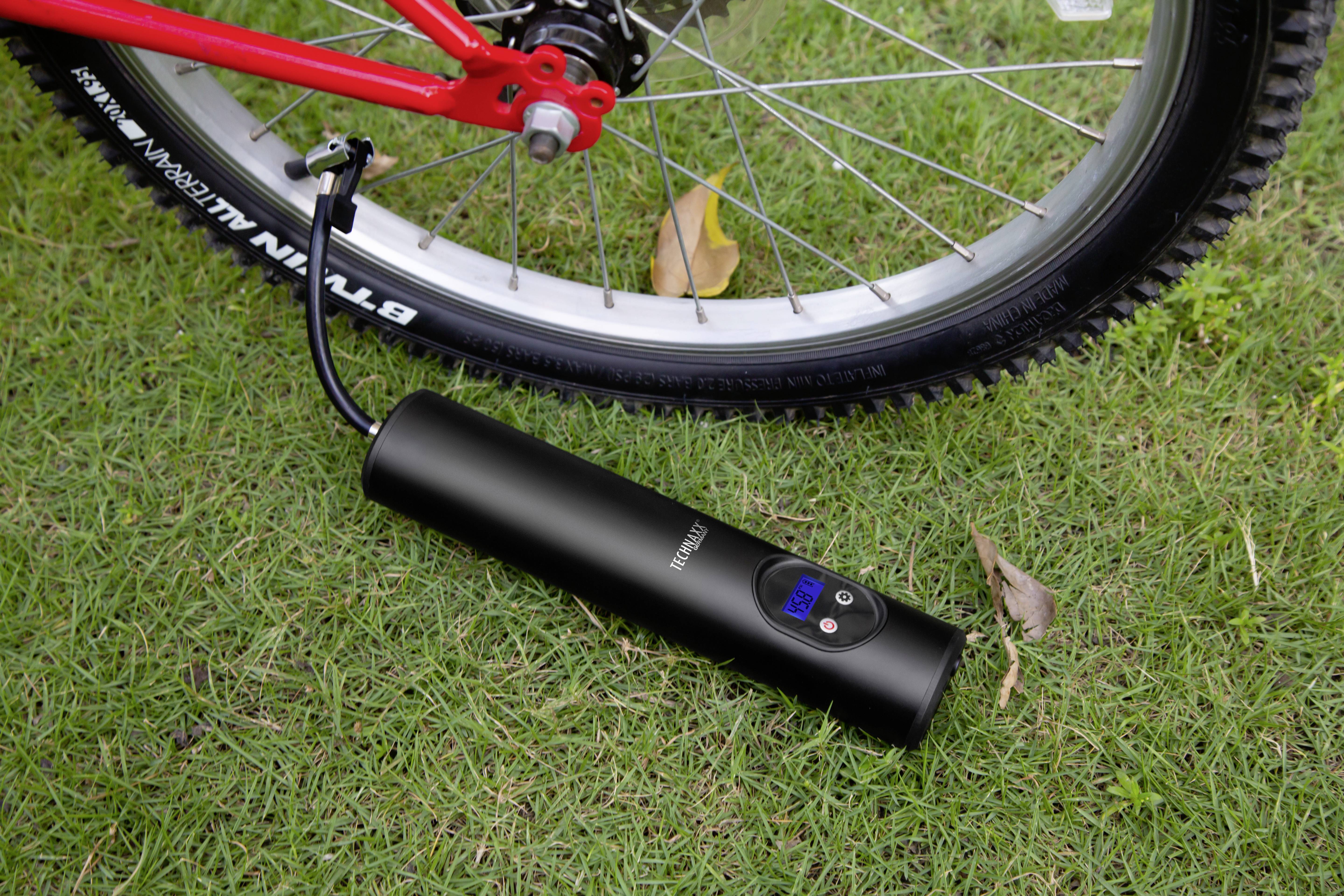 Zwarte draagbare compressor pompt een fietsband op groen gras. De digitale weergave op de compressor toont de druk.