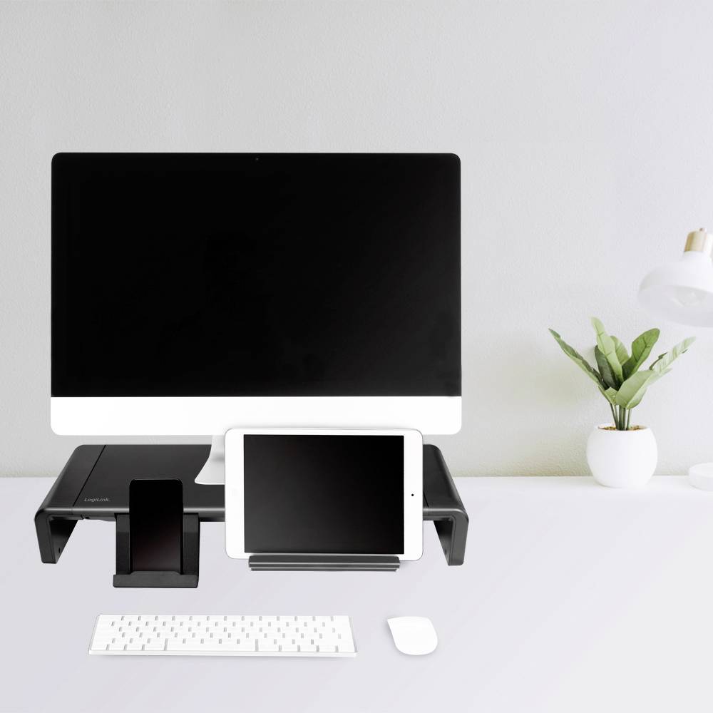Een bureau met computer, tablet, smartphone, toetsenbord en muis. Rechts een plant en een lamp. Moderne kantoorinrichting.