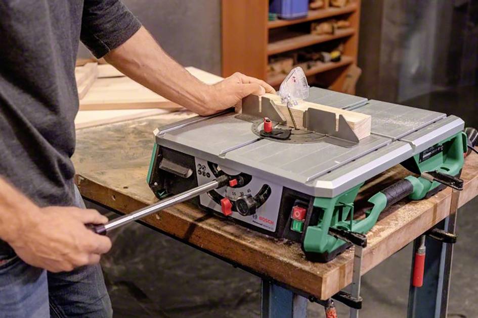 Een persoon bedient een tafelcirkelzaag in een werkplaats. Een stuk hout wordt gesneden met behulp van een hoekgeleider.