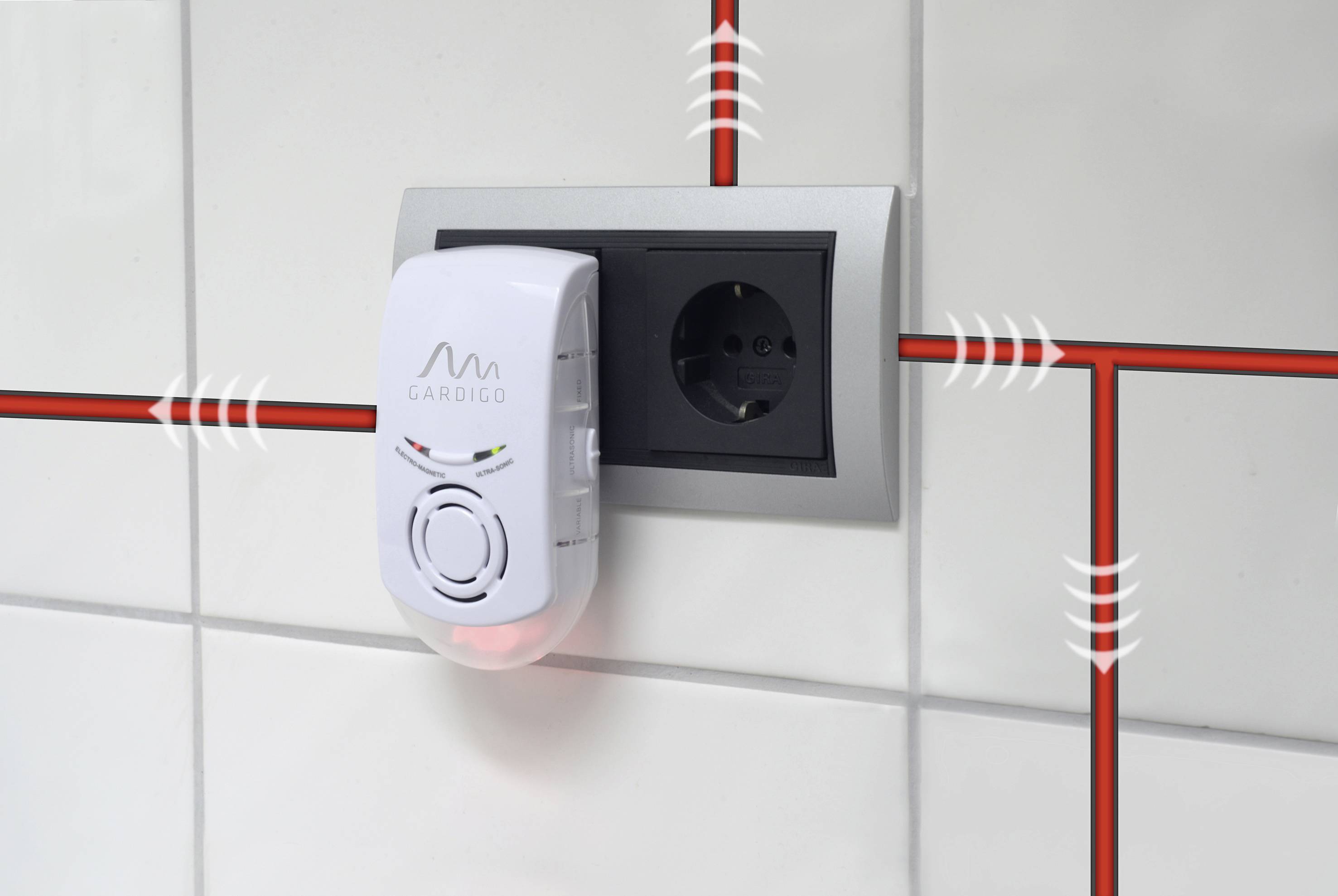 Een witte elektrische ongedierteafweerder is aangesloten op een stopcontact aan een betegelde muur. Golvende lijnen symboliseren ultrasoon geluid.