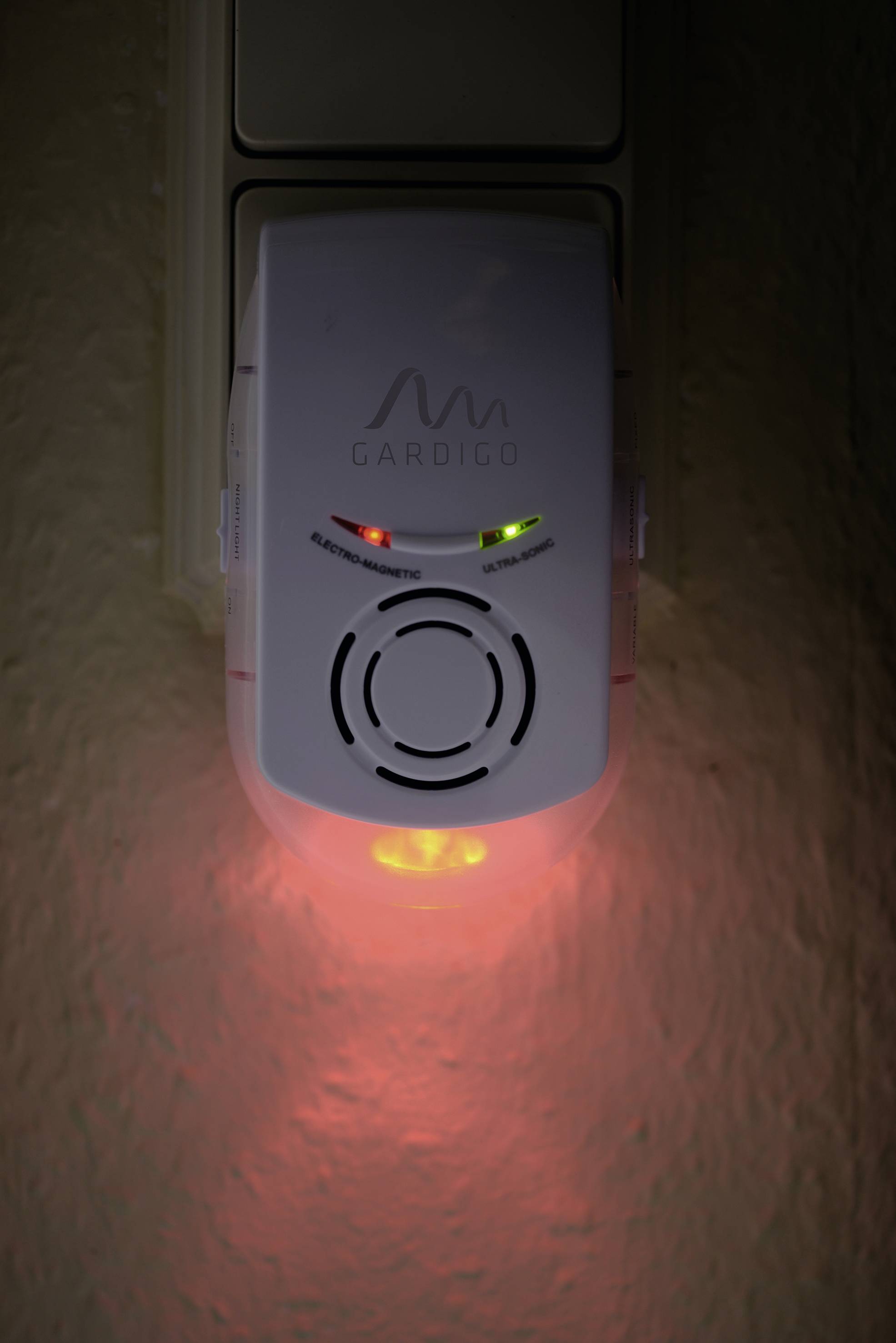 Een elektronisch apparaat met een rode verlichte indicator, gestoken in een stopcontact. Het heeft twee extra groene lichten.