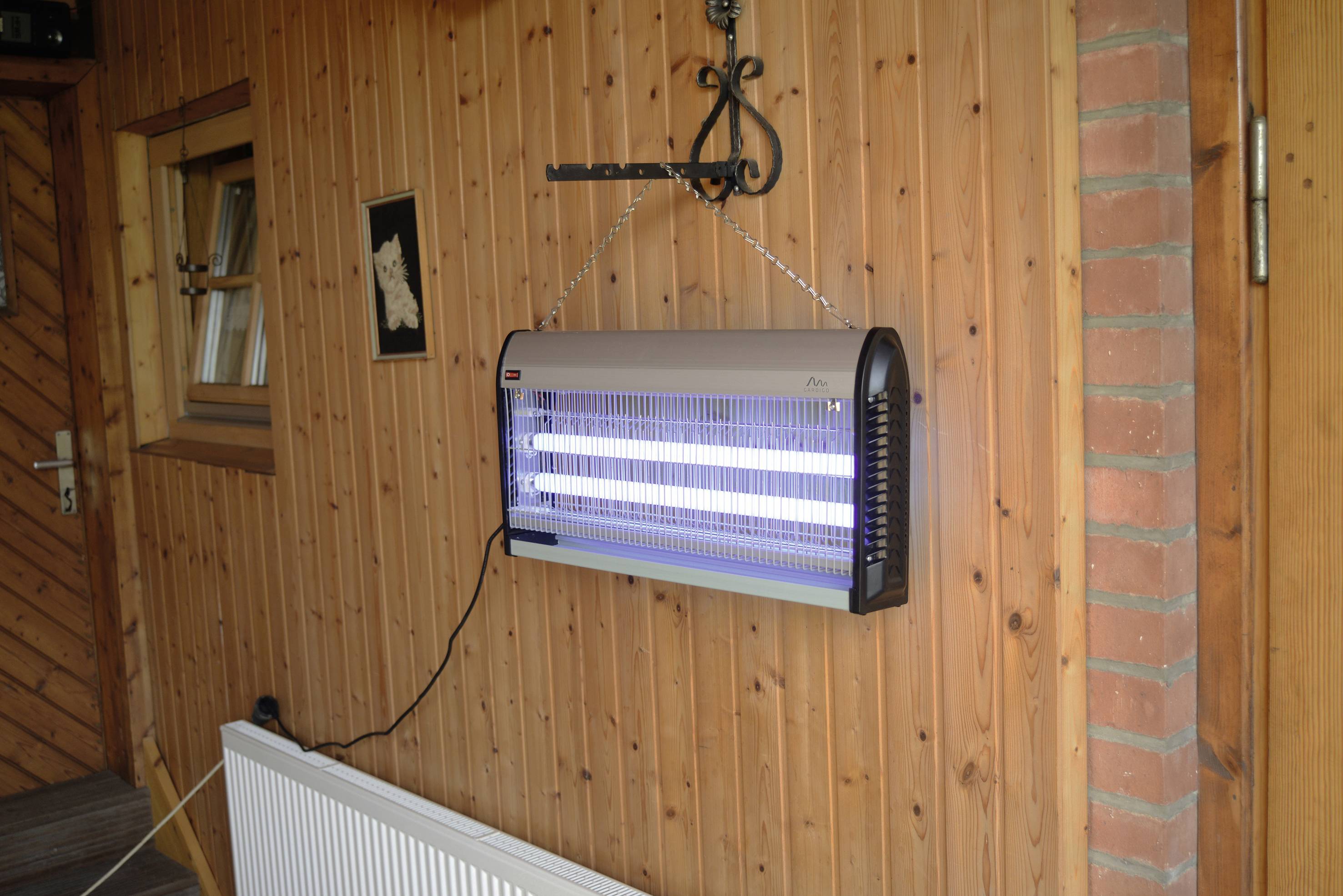 Elektrische insectenverdelger met twee lichtbuizen hangt aan een houten muur in een buitenruimte.