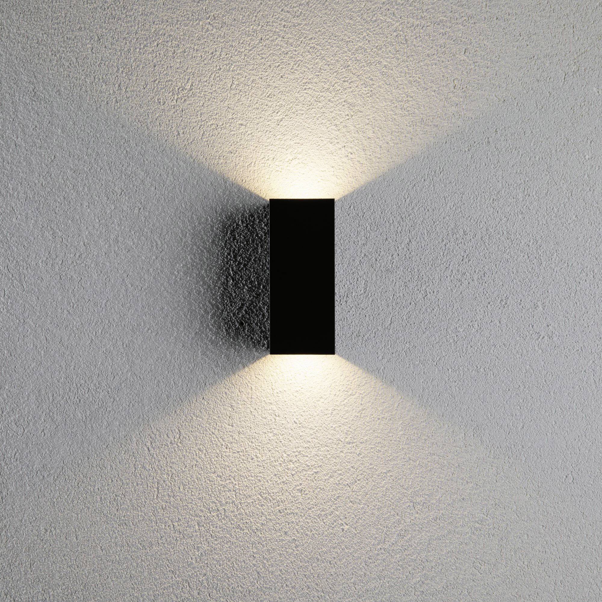 Wandlamp straalt warm licht naar boven en beneden op een grijze muur en creëert een symmetrisch patroon.