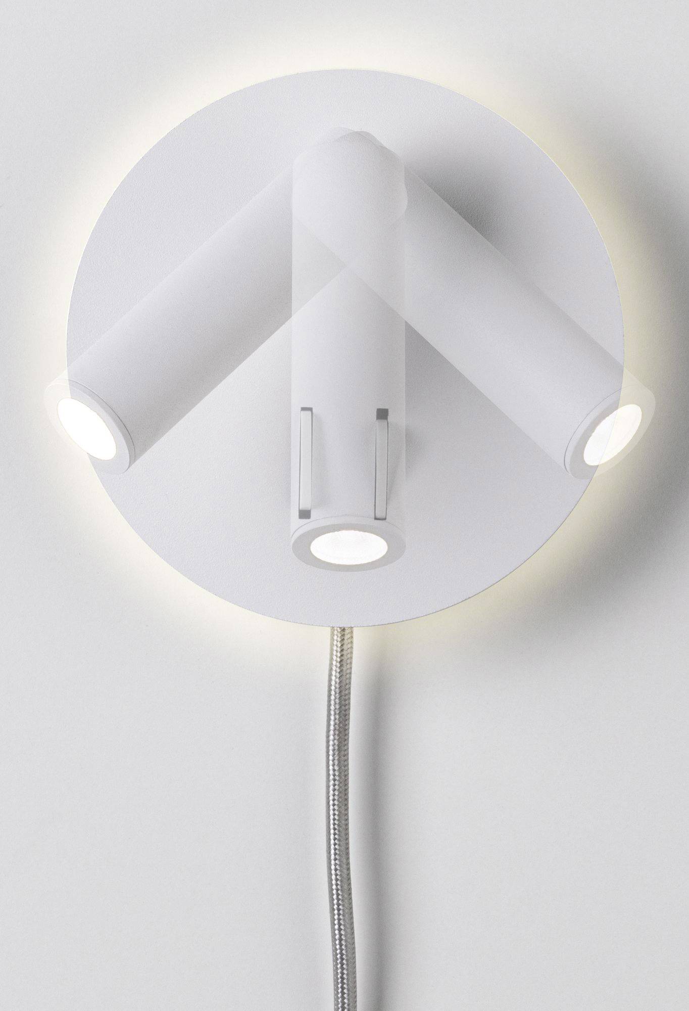 Een witte wandlamp met drie verstelbare lichtbronnen verspreidt zacht licht. De lamp heeft een modern design.