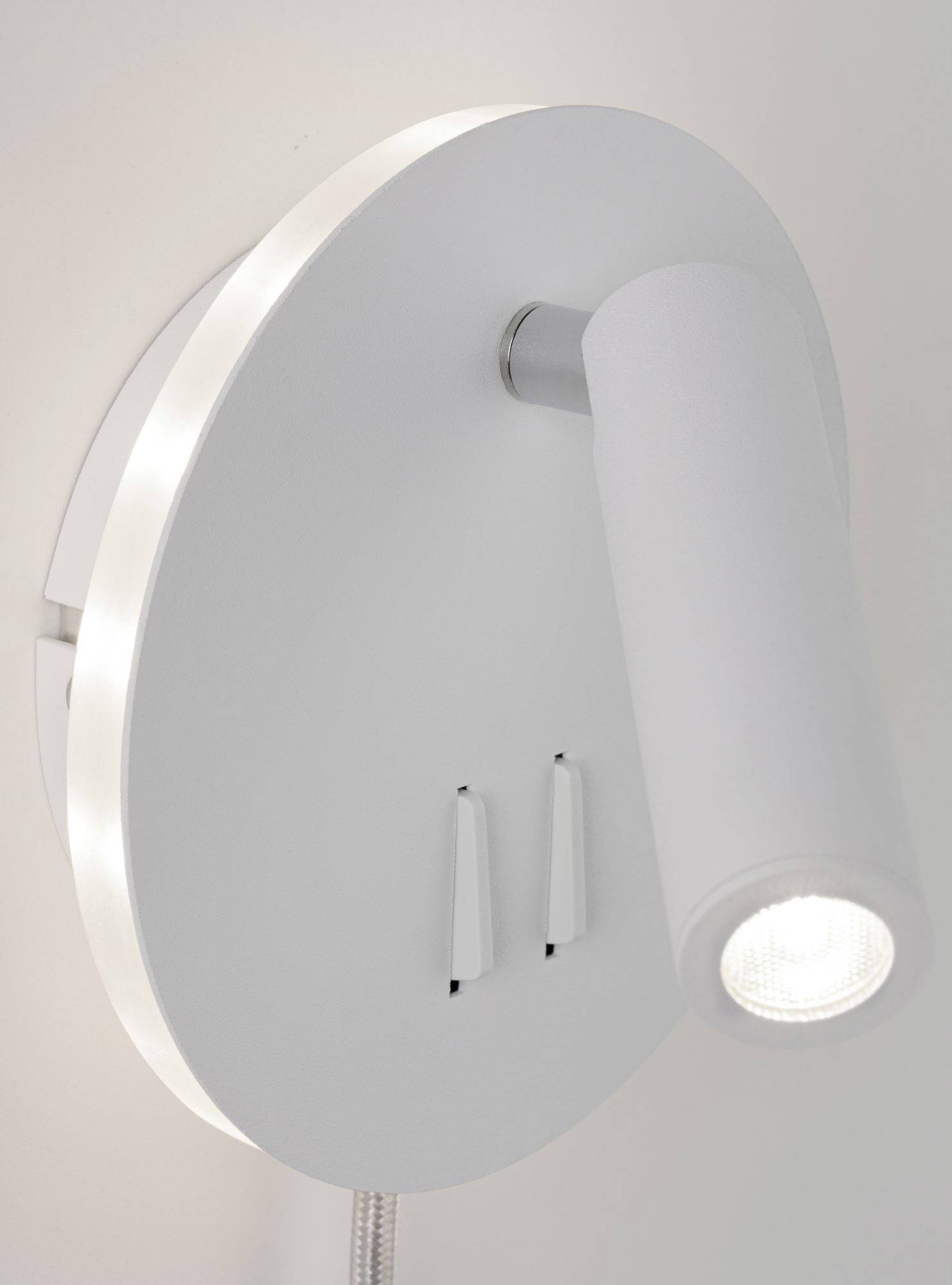 Wandlamp met een ronde voet en een cilindrische spot, die zijdelings verlicht. Twee schakelaars eronder, gemonteerd op een witte muur.