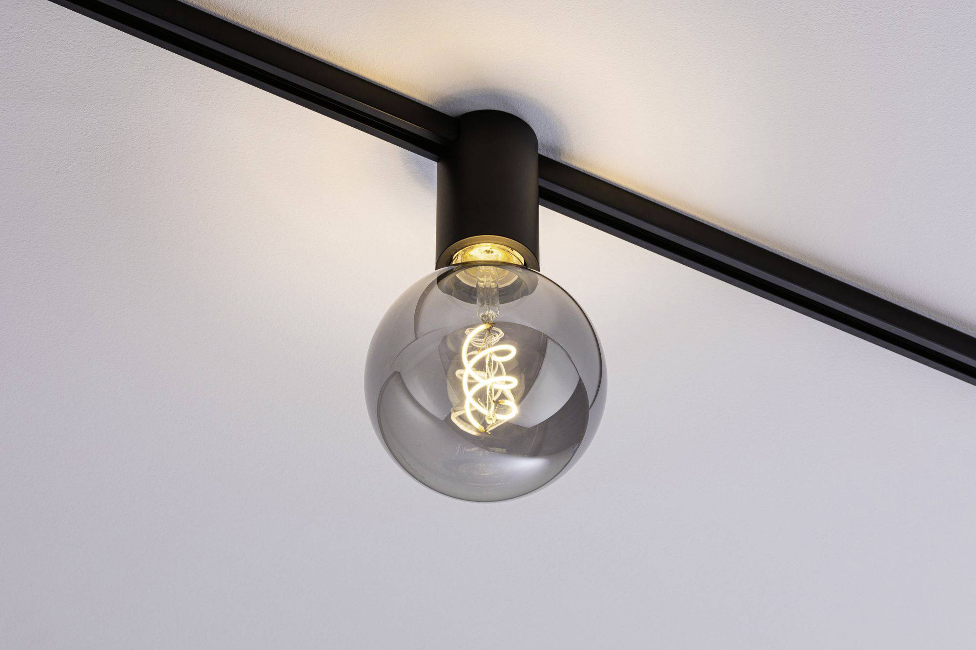 Een moderne, ronde gloeilamp aan een zwarte plafondlijst. De lamp geeft zacht licht en zorgt voor een zachte sfeer in de ruimte.