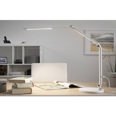 Een moderne bureau met een witte led-lamp, opengeslagen boeken en planken op de achtergrond. Een schilderij aan de muur.