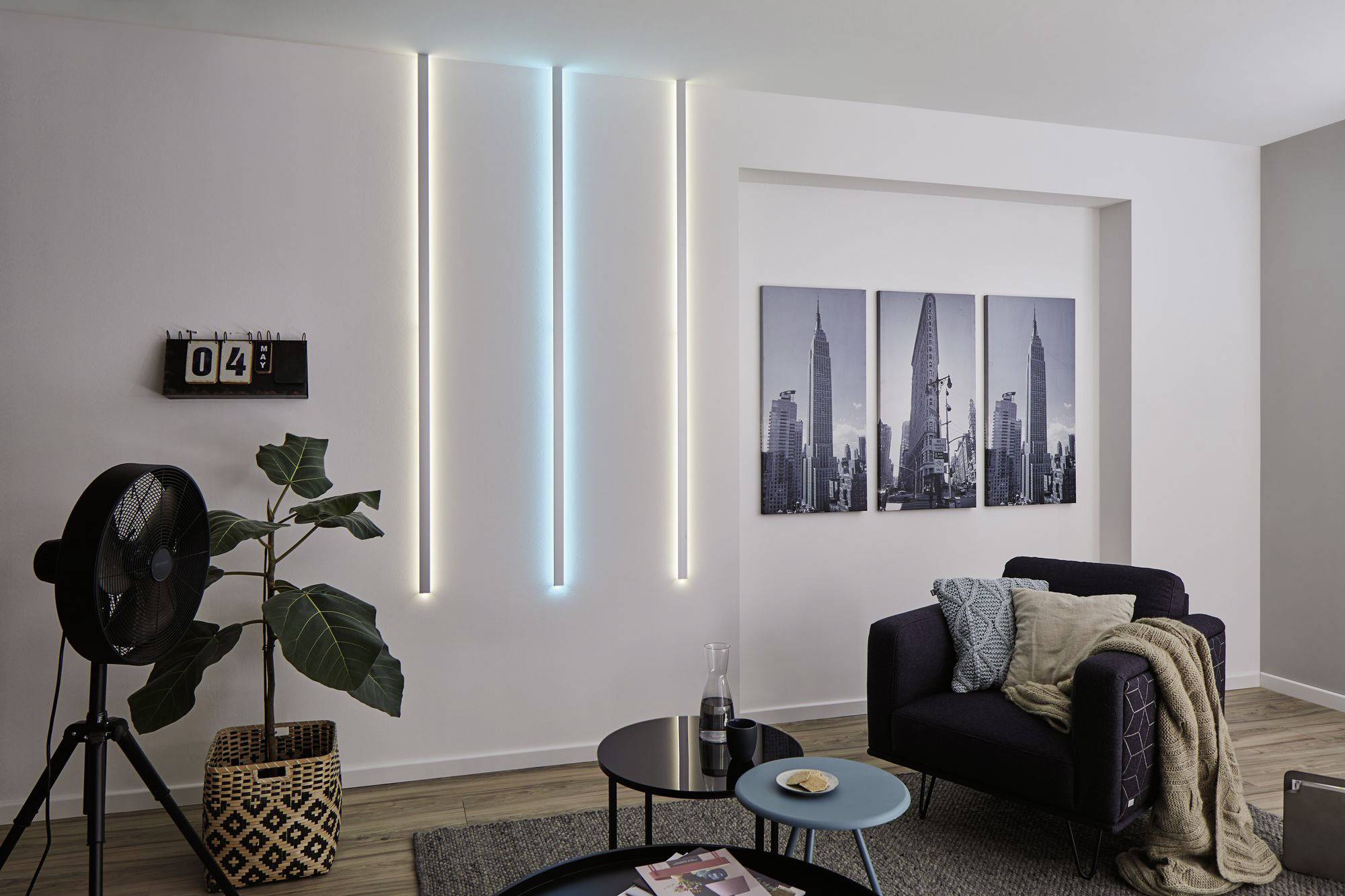 Woonkamer met modern decor: wandverlichting met blauwe en witte led-strips, planten, tafel en bank, stadslandschapskunstwerk aan de muur.