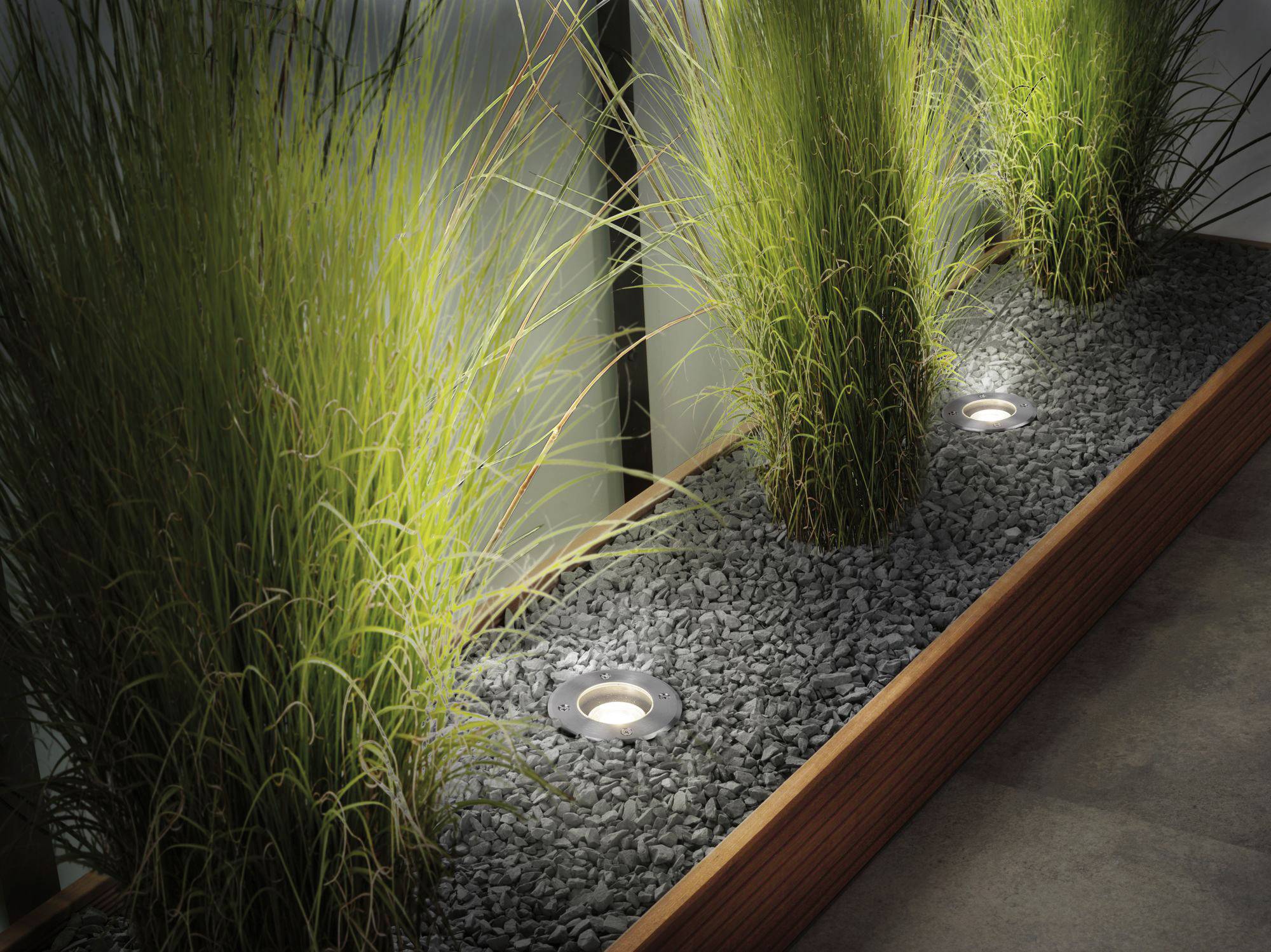 Groen siergroen groeit in een bloemperk gevuld met grijze stenen, verlicht door in de grond ingebouwde verlichting.