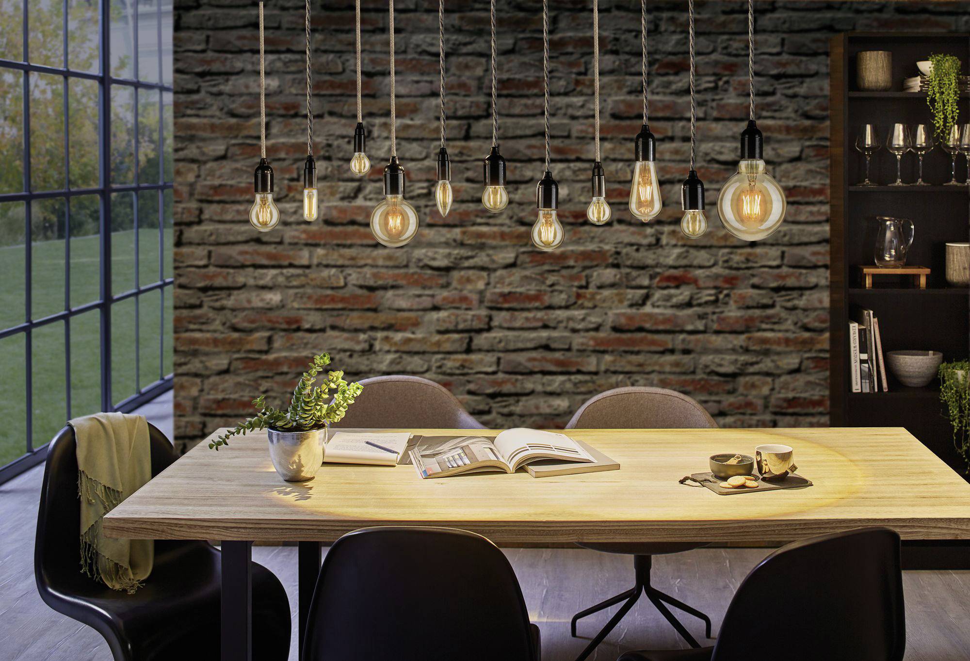 Eetkamer met een houten tafel, vier stoelen en opengeslagen boeken. Hangende lampen verlichten de ruimte. Raam en rek op de achtergrond.