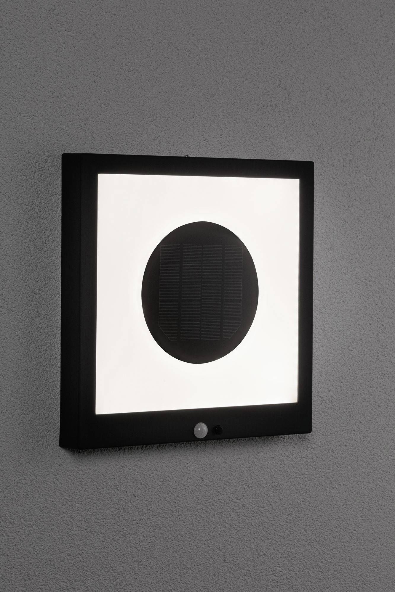 Een vierkante lamp met een zwarte rand en een cirkelvormig licht in het midden, gemonteerd aan een grijze muur.