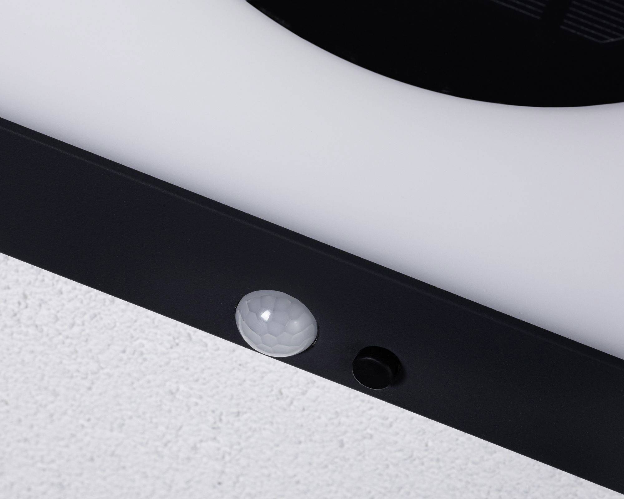 Plafondlamp met geïntegreerde ronde sensor, gemonteerd in een modern, zwart frame aan een witte plafond.
