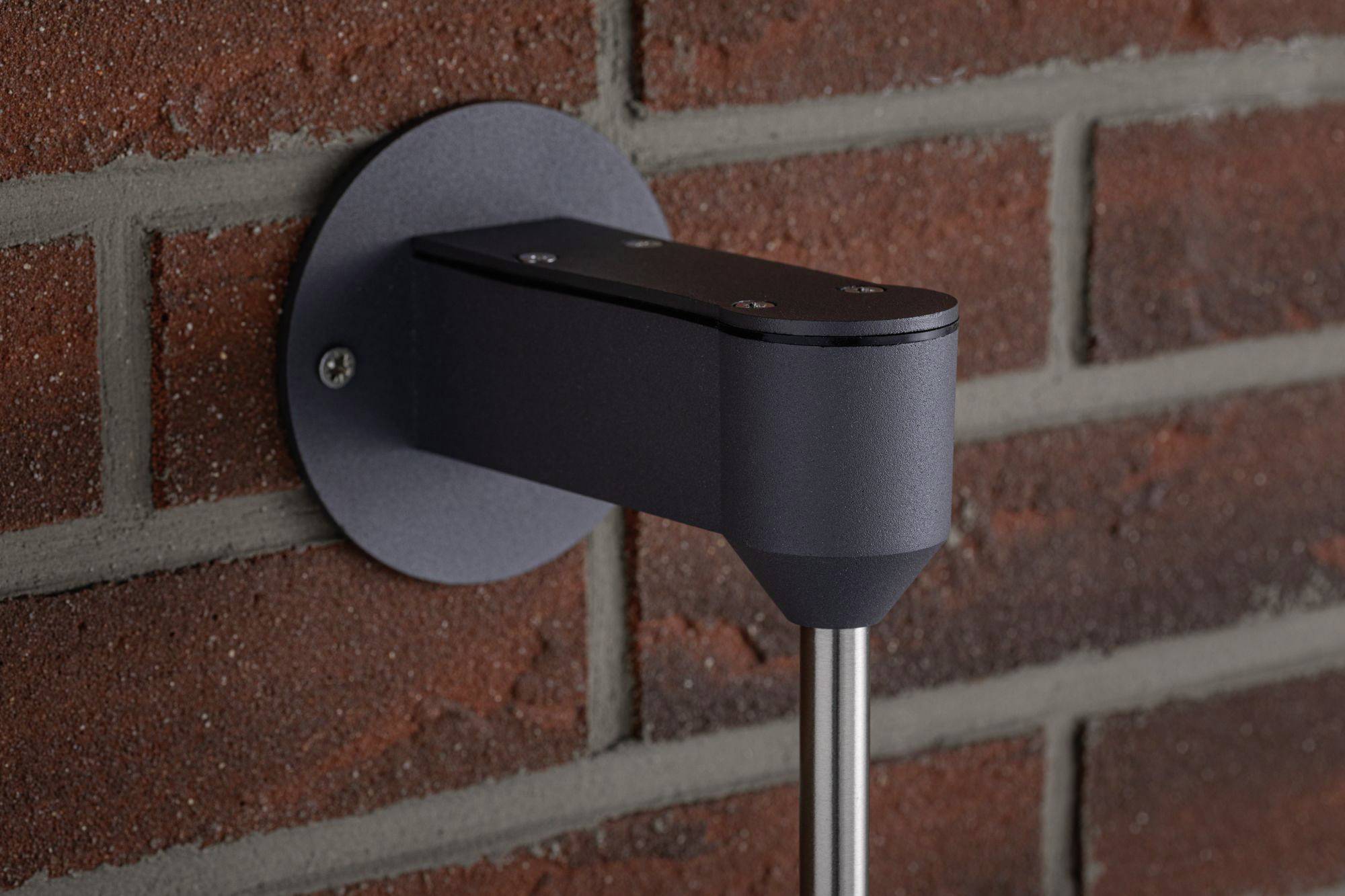 Zwarte wandsteun met zilveren staaf, gemonteerd aan een roodbruine bakstenen muur.