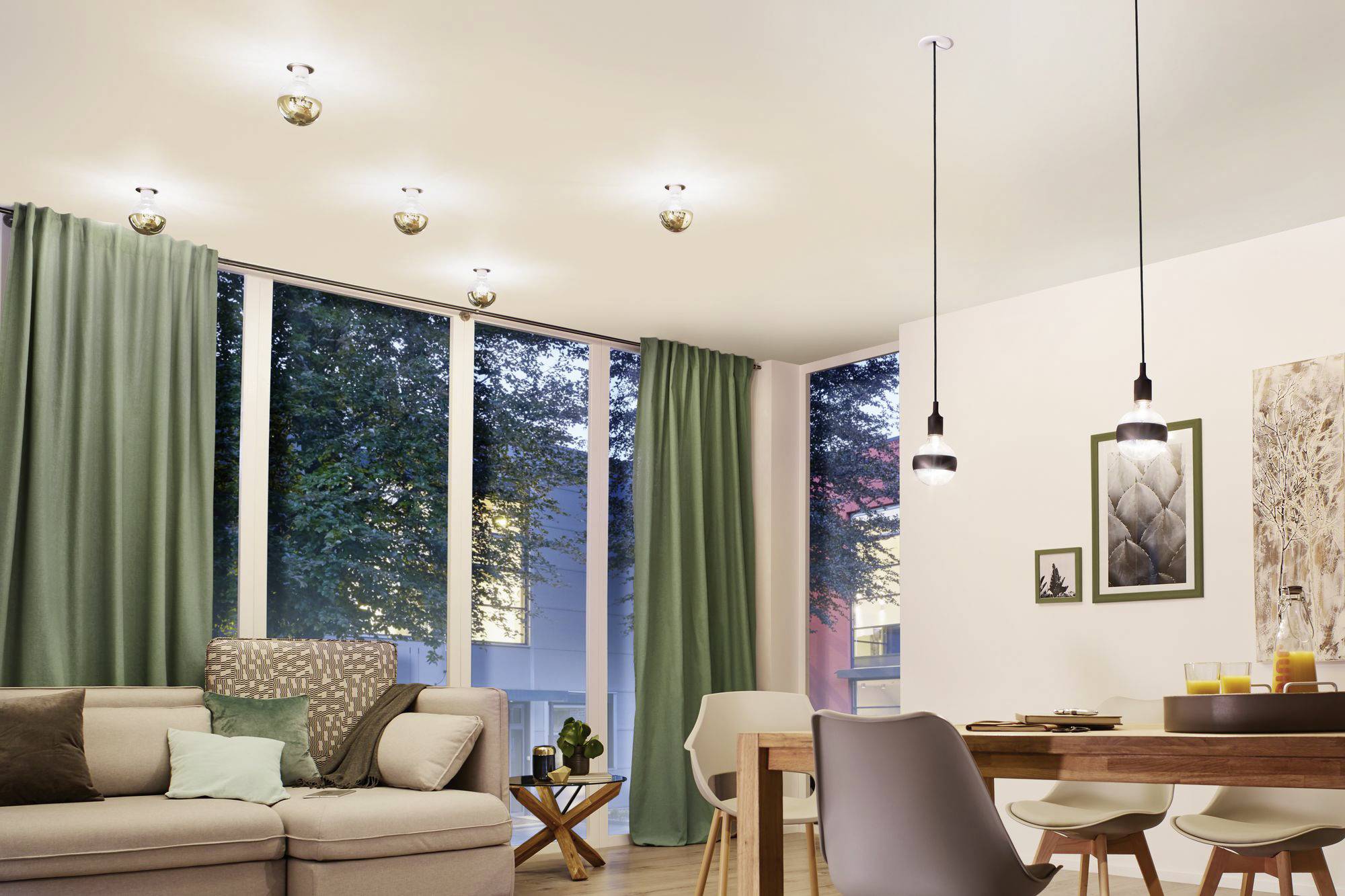 Een helder verlichte woonkamer met moderne hanglampen, een beige bank, grote ramen met groene gordijnen en een eettafel.