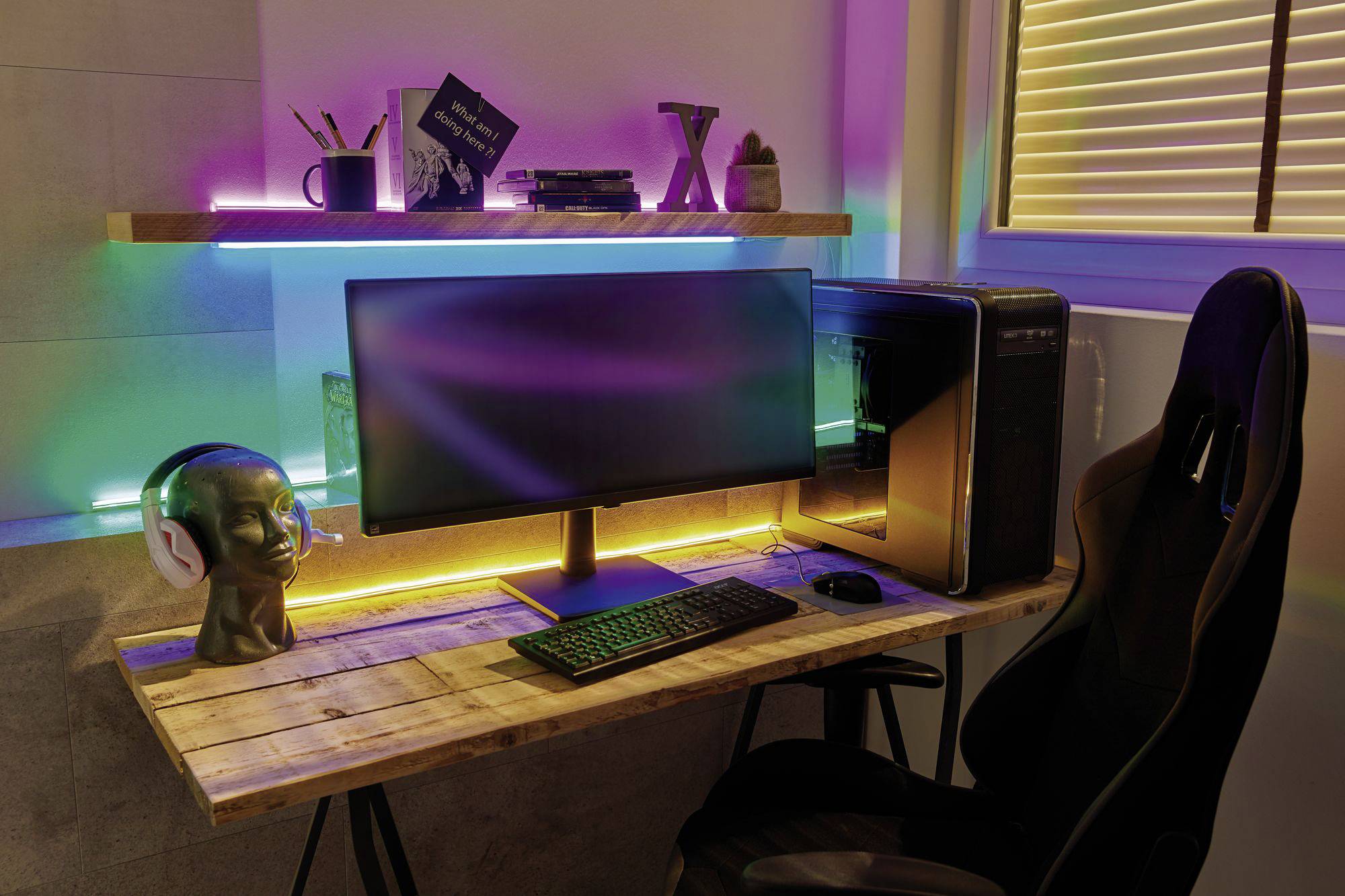 Een bureau met een computer, toetsenbord, muis en koptelefoon op een modelkop. Kleurrijke LED-strips creëren decoratieve verlichting.