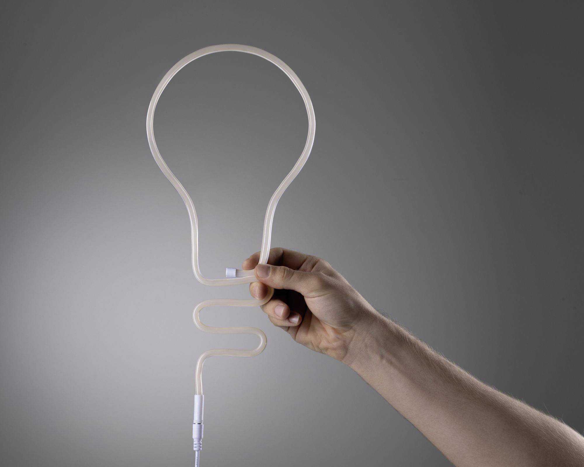 Een hand houdt een LED-lamp in de vorm van een gloeilamp tegen een grijze achtergrond. De lamp toont een creatief ontwerp.