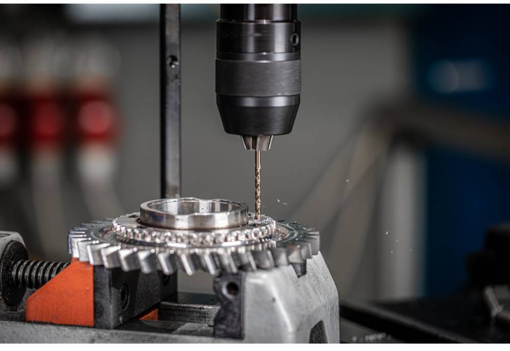Close-up van een boor die een metalen tandwiel bewerkt in een werkplaats.