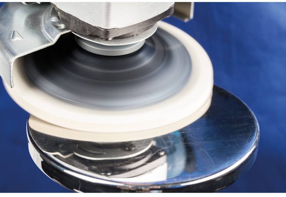 Een polijstmachine met een ronddraaiend pad polijst een metalen oppervlak. De achtergrond is blauw.