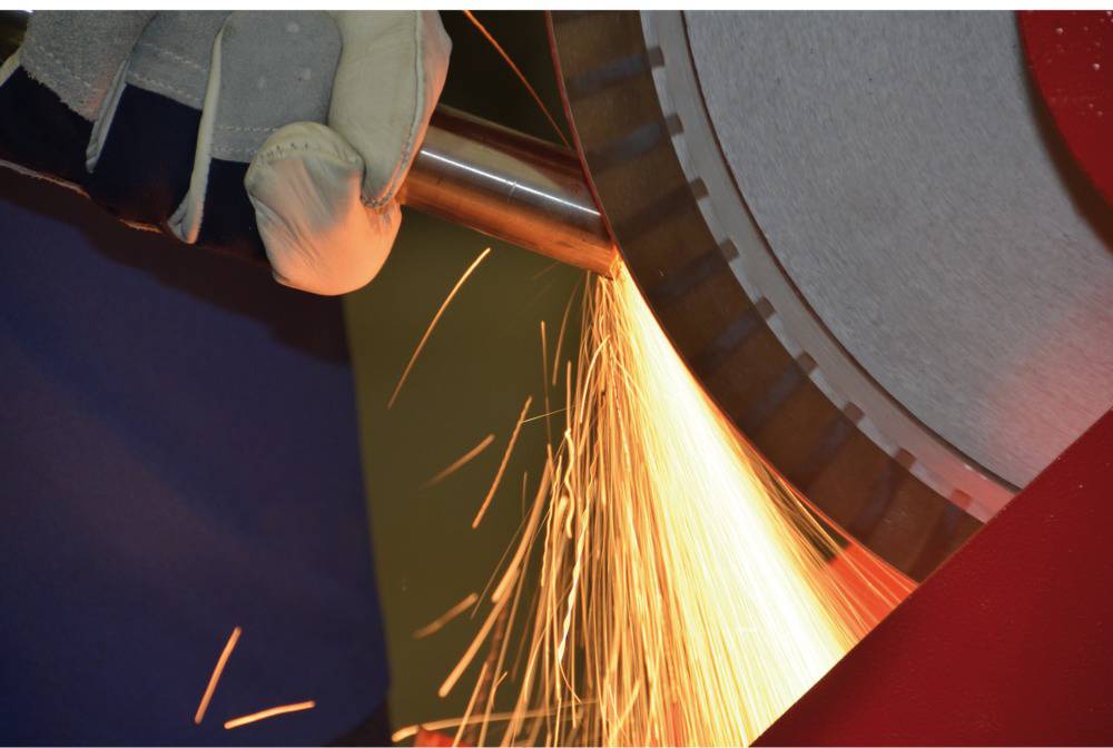 Vonken spatten rond van een metalen slijpschijf terwijl iemand met beschermende handschoenen aan het werk is.