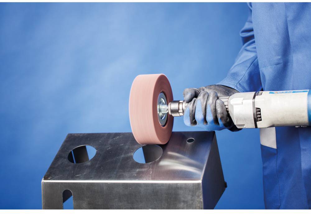 Een persoon in blauwe werkkleding slijpt een metalen plaat met een roterende slijpmachine, achtergrond in blauw gehouden.