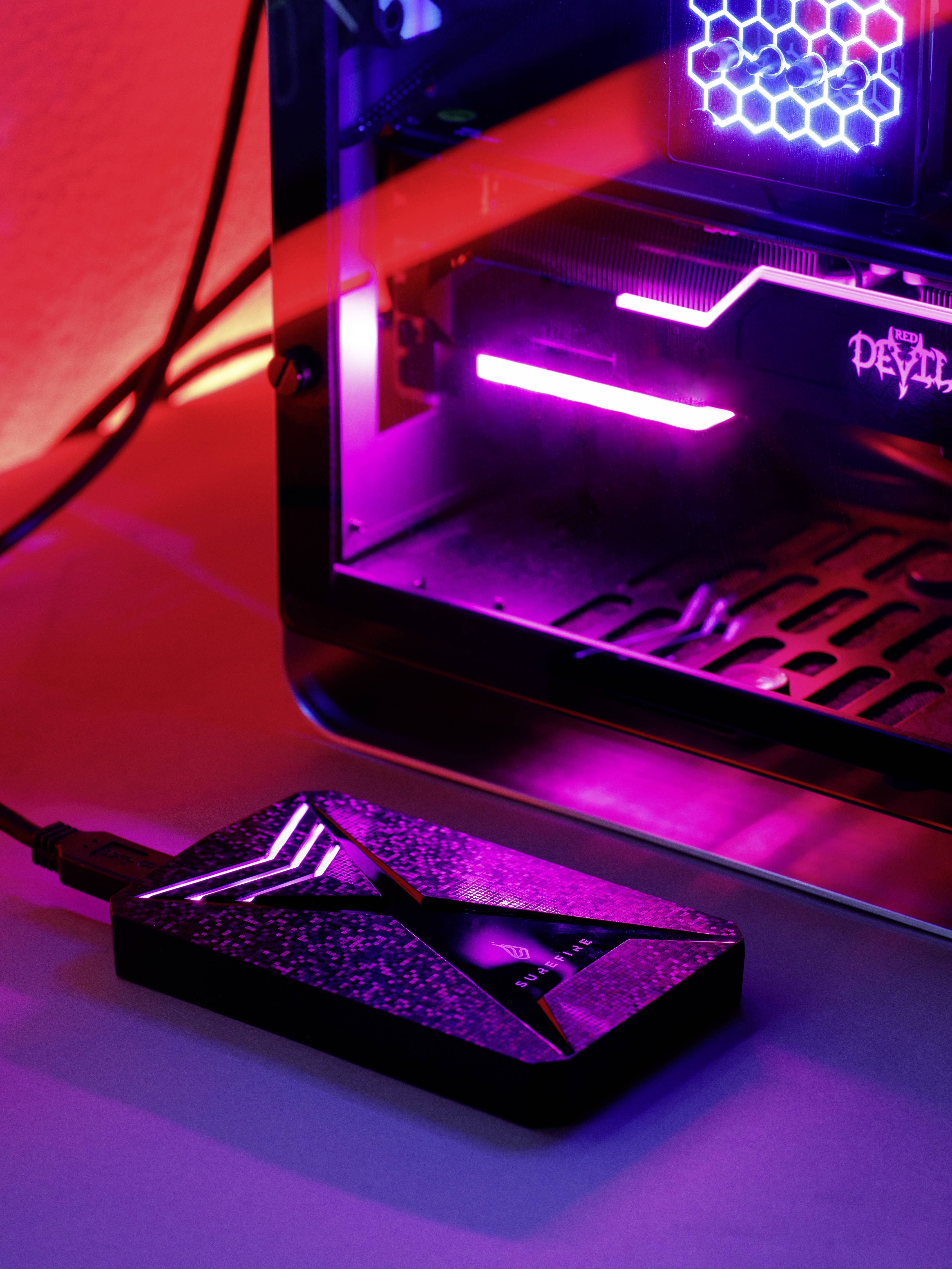 Een externe opslag in modern design ligt naast een verlicht pc-behuizing met rode en paarse lichteffecten.