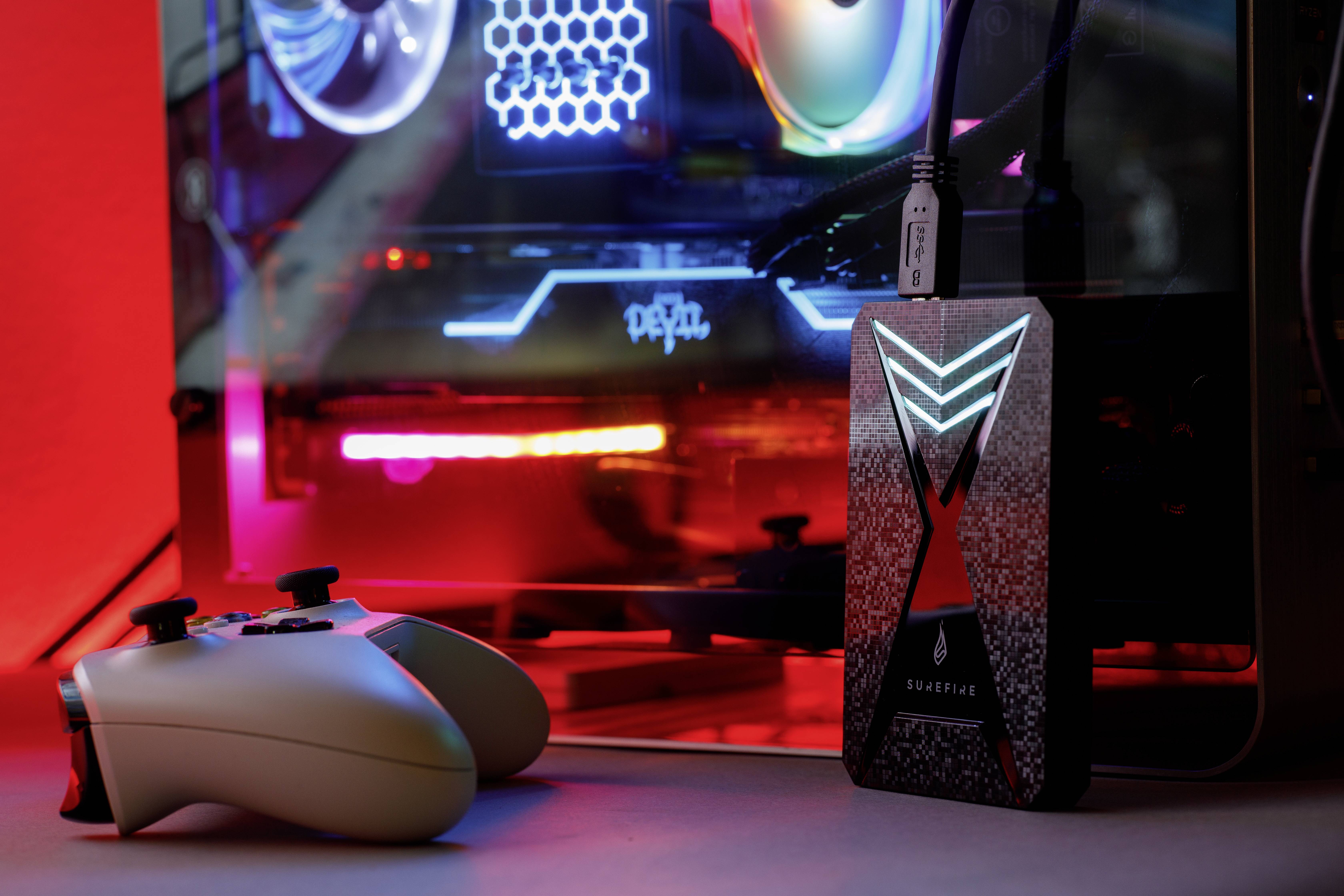 Een gamingcomputer met verlichte ventilatoren en een externe harde schijf; op de voorgrond liggen twee gamecontrollers.