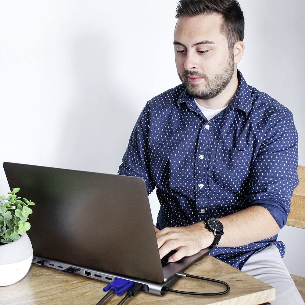 Een man zit aan een tafel en werkt op een laptop. Naast hem staat een kleine plant.