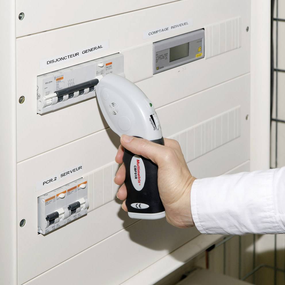 Een persoon houdt een infrarood-thermometer voor een zekeringkast om de temperatuur van stroomcircuitschakelaars te meten.