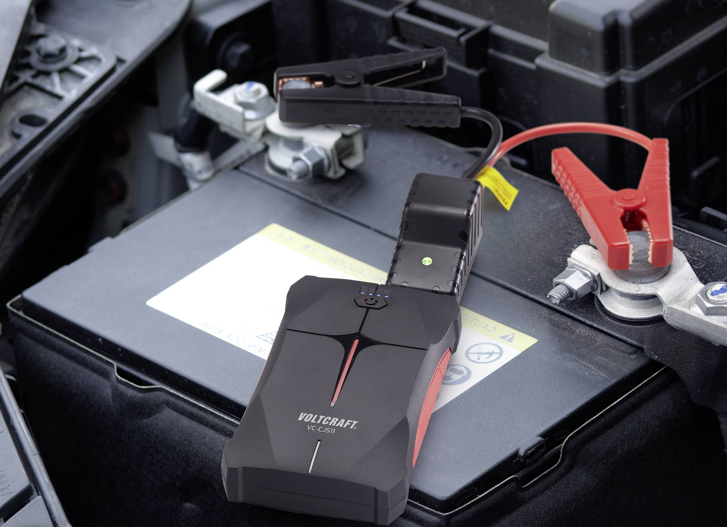 'Draagbare starthulpset aangesloten op autoaccu. Zwarte en rode klemmen zijn bevestigd aan de accupolen.'