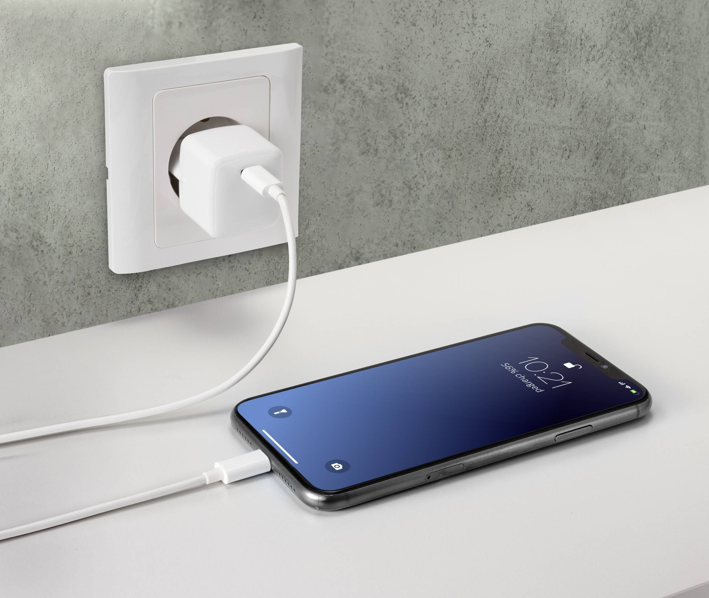 Een smartphone ligt op een tafel en is via een oplaadkabel aangesloten op een stopcontact. Het scherm toont de tijd 10:21.