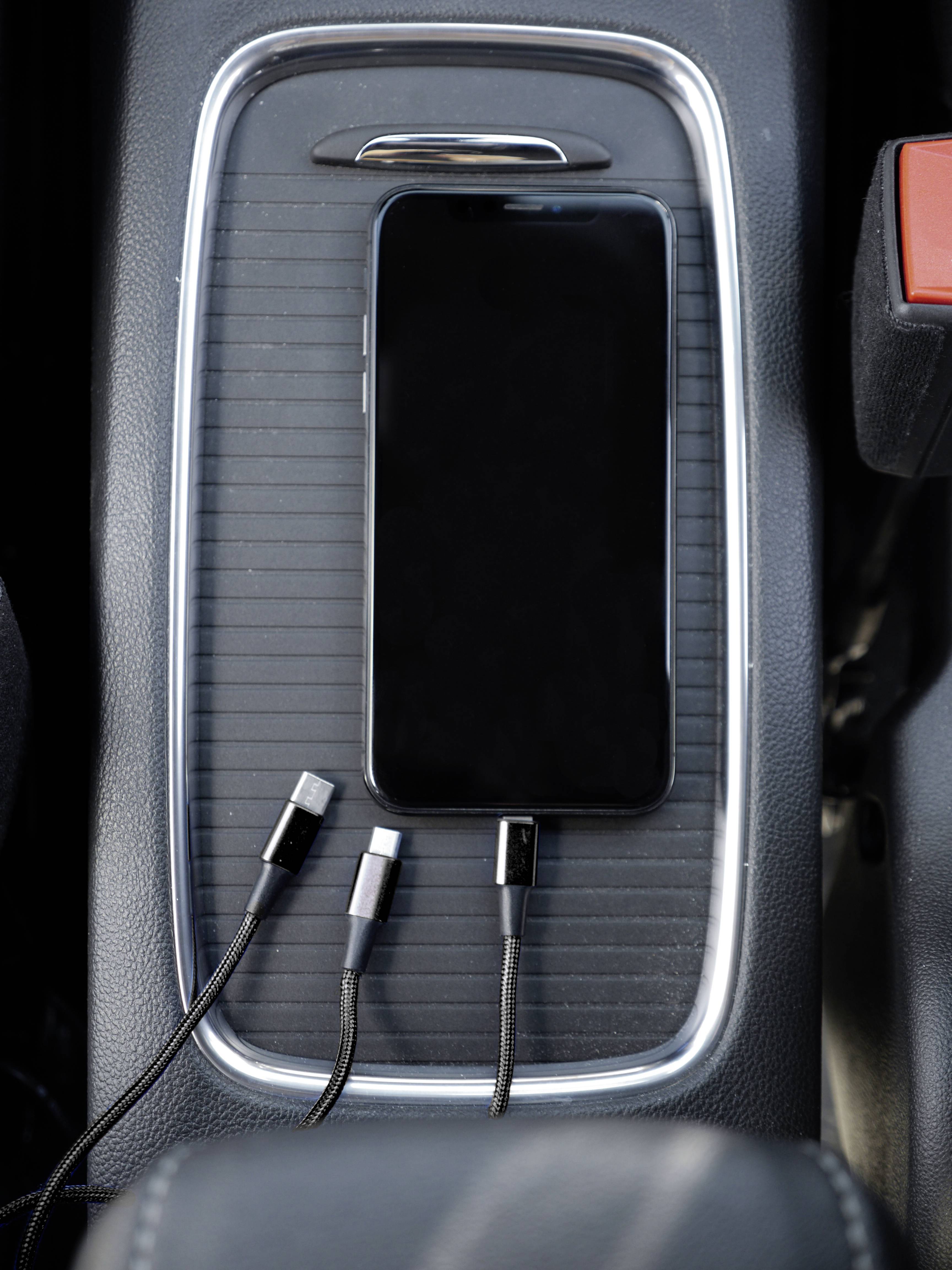 Een smartphone ligt op de middenconsole van de auto, naast drie verschillende oplaadkabels.