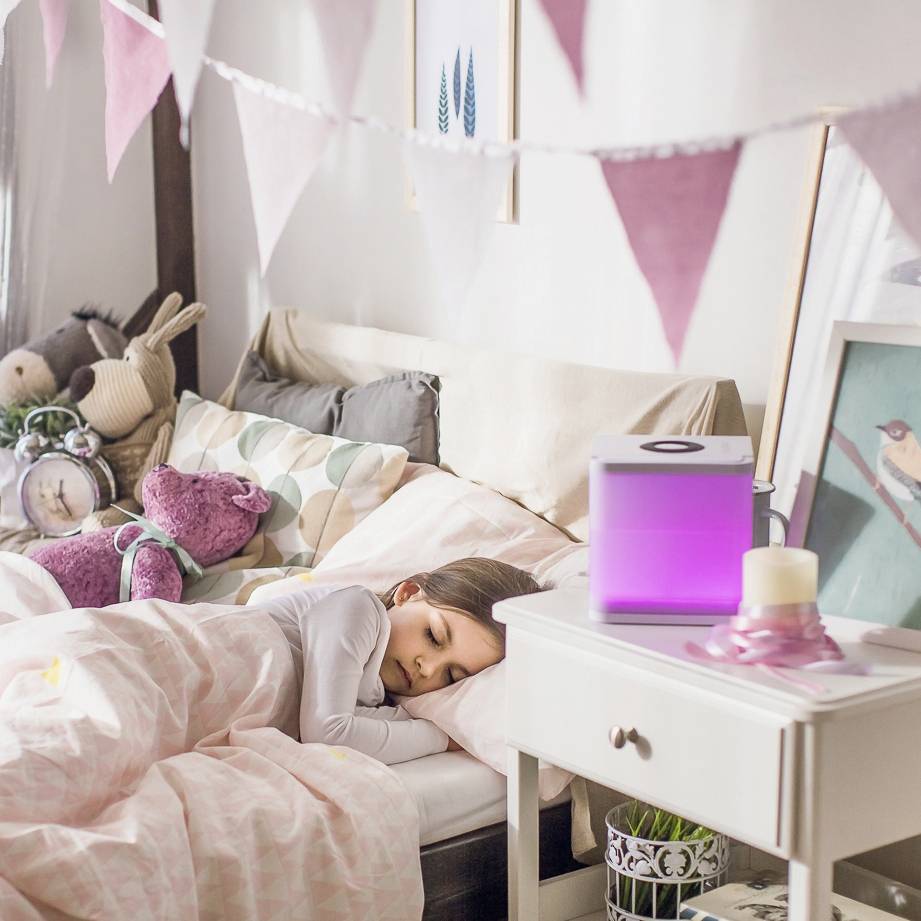 Een kind slaapt vredig in een bed met zachte beddengoed en knuffels, omgeven door zacht licht en decoratieve slingers.