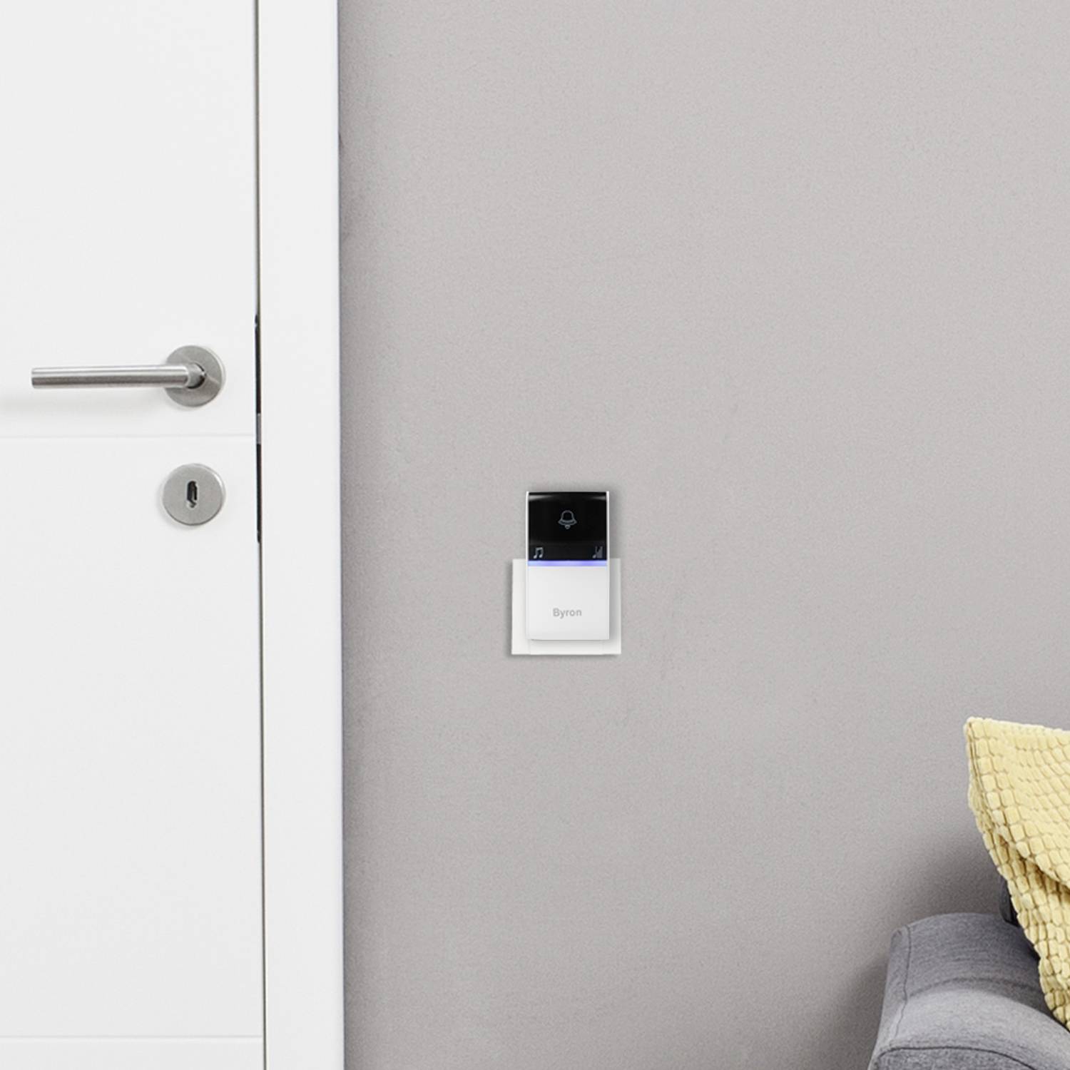 Een witte deur met een zilveren handgreep en slot staat licht open. Naast de muur hangt een thermostaat en rechts is een deel van een bank zichtbaar.