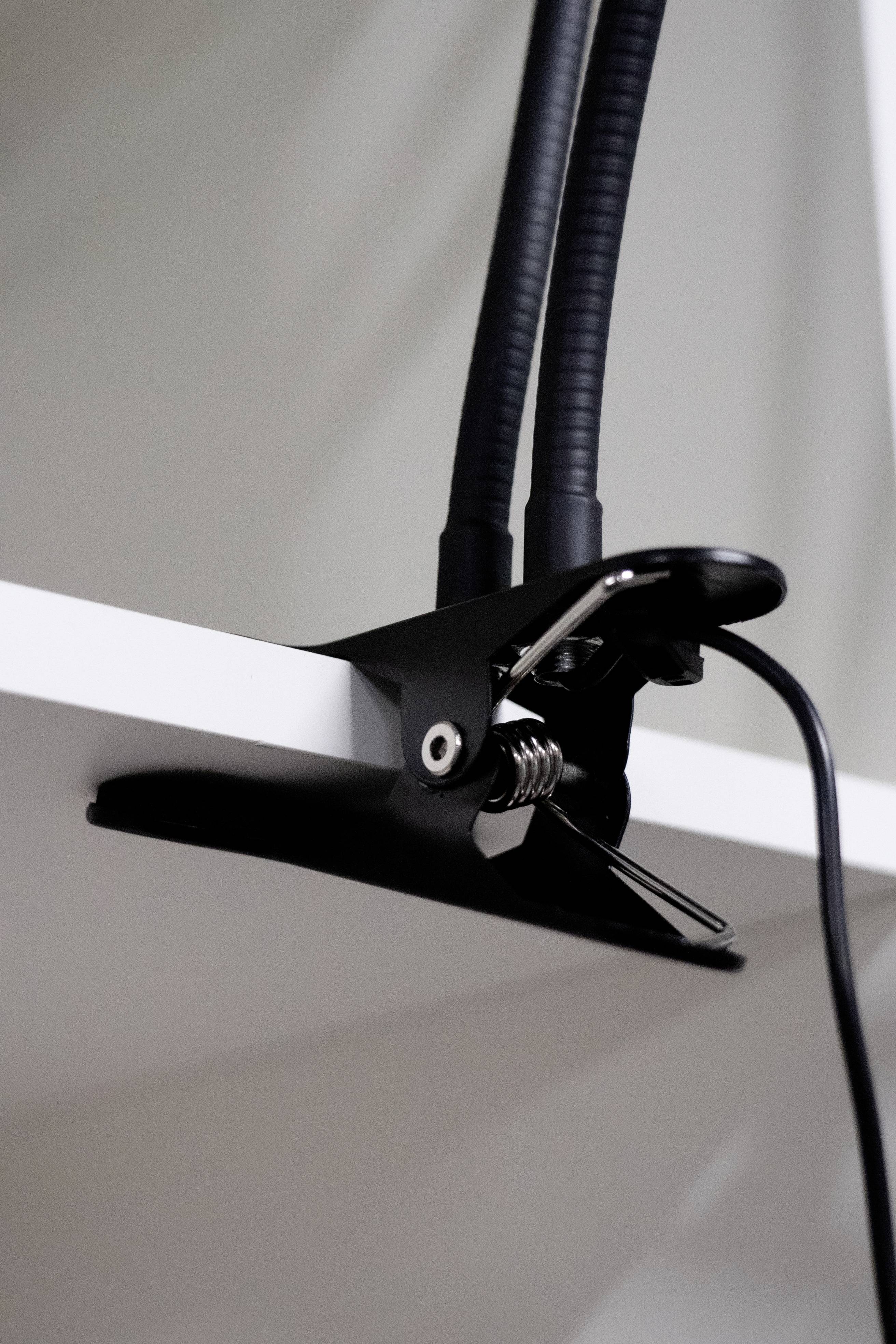 Een zwarte klem houdt een lamp vast aan een witte tafelrand. Een kabel hangt neer van de klem.