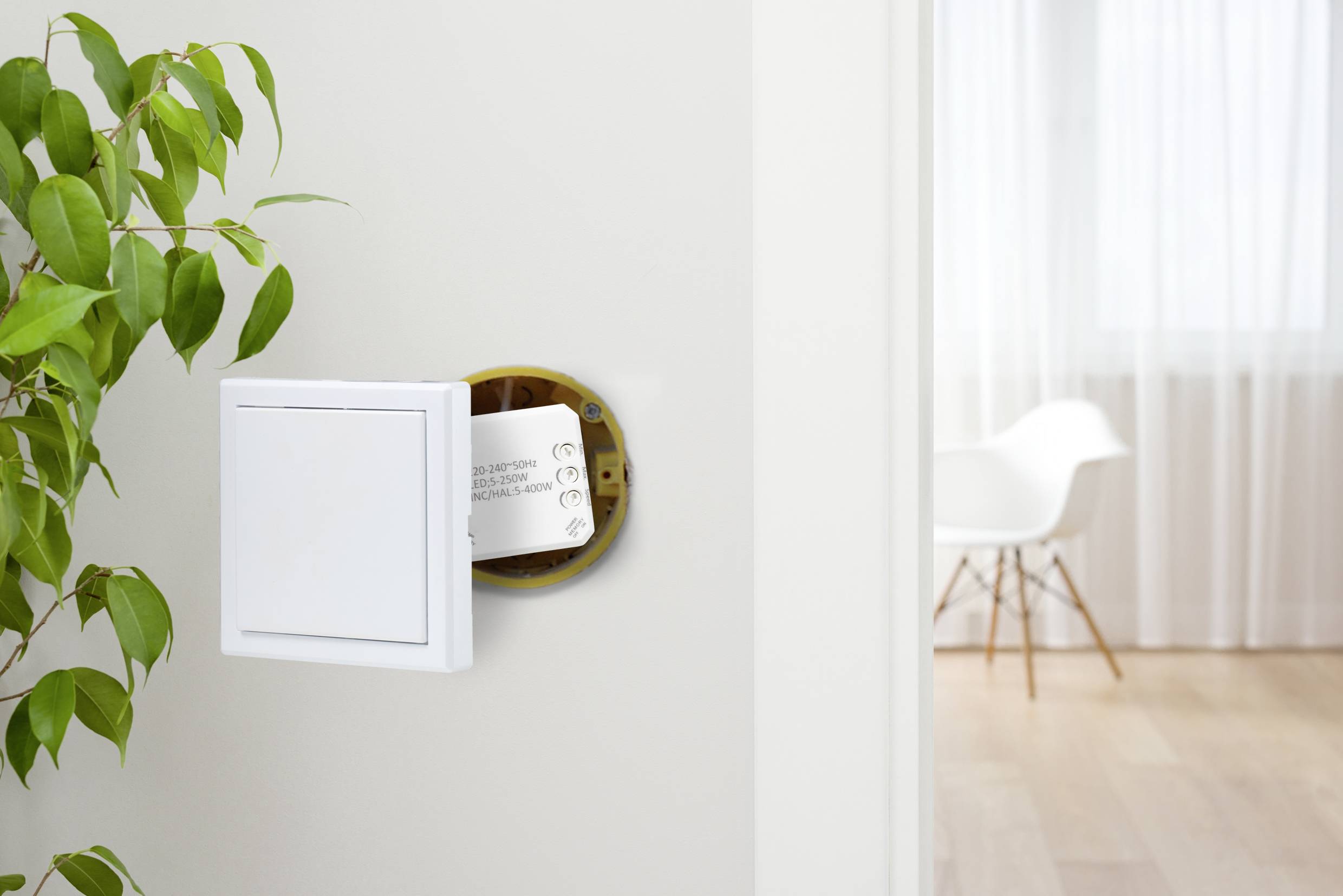 Lichtschakelaar aan de muur, deels opengeklapt, toont een gedrukt papier aan de binnenkant. Links een groene plant, op de achtergrond een lichte ruimte.