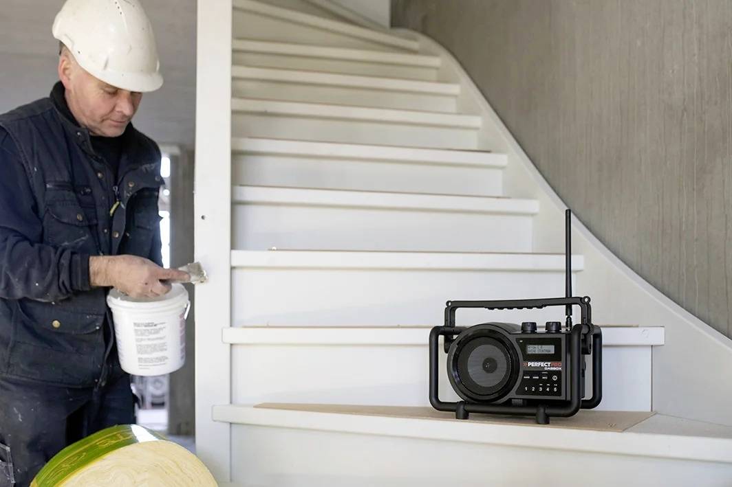 Een bouwvakker met een witte helm schildert een trap. Op de trap staat een bouwradio.