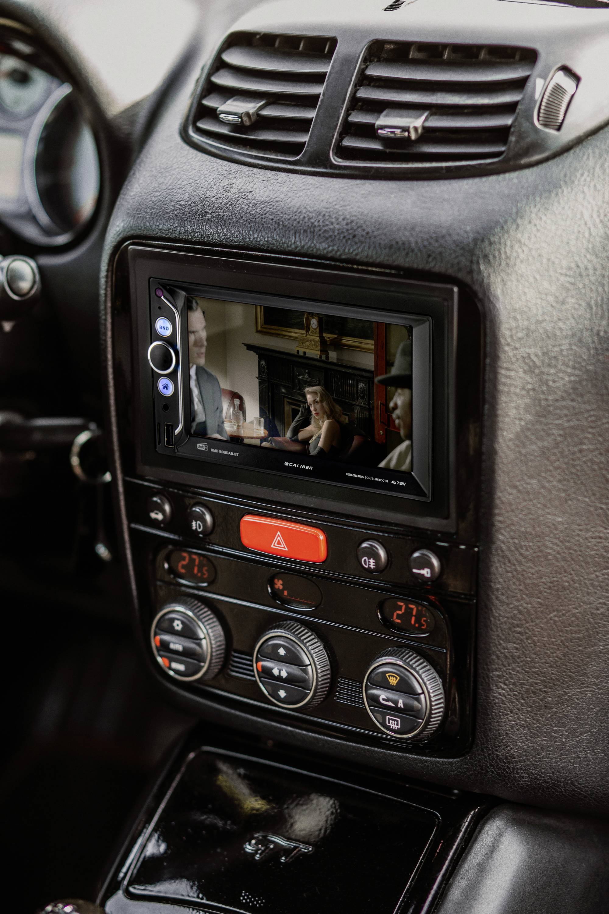 Navigatiesysteem van een auto toont een film op het scherm, omgeven door ventilatiesleuven en klimaatregelingsknoppen.