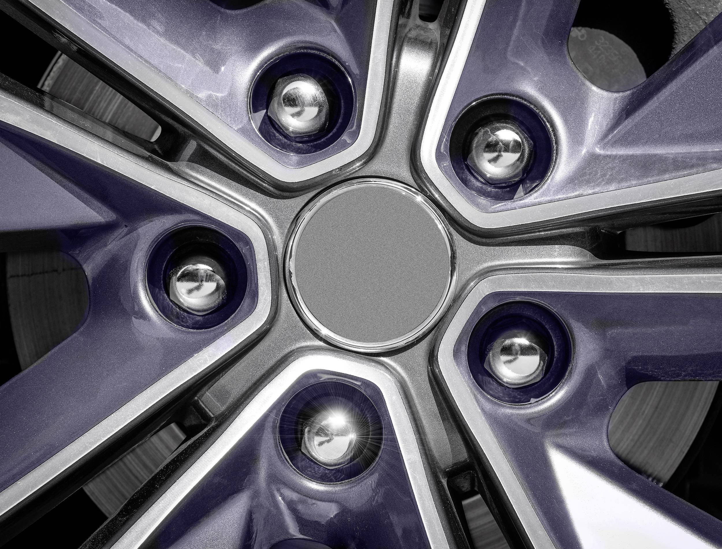 Close-up van een autoremschijf met gestileerde velgen, zilveren moeren en een geometrisch patroon in donkergrijs en zilver.