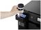 Een hand vult een printer met inkt uit een fles. De printer toont meerdere inktcartridges.
